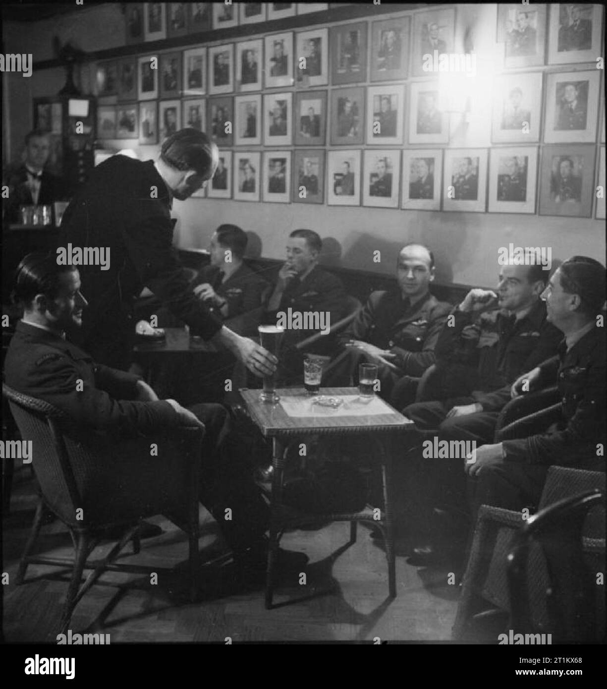 Belgian Clubs and Cafes in London- Rest, Relaxation and Entertainment, London, England, UK, 1945 Belgian pilots enjoy a beer, a cigarette and a chat as they relax at 'Aux Neufs Provinces', a club attached to the restaurant 'Chez Gaston', near Victoria Station. The wall behind them is lined with portrait photographs of airmen. Stock Photo