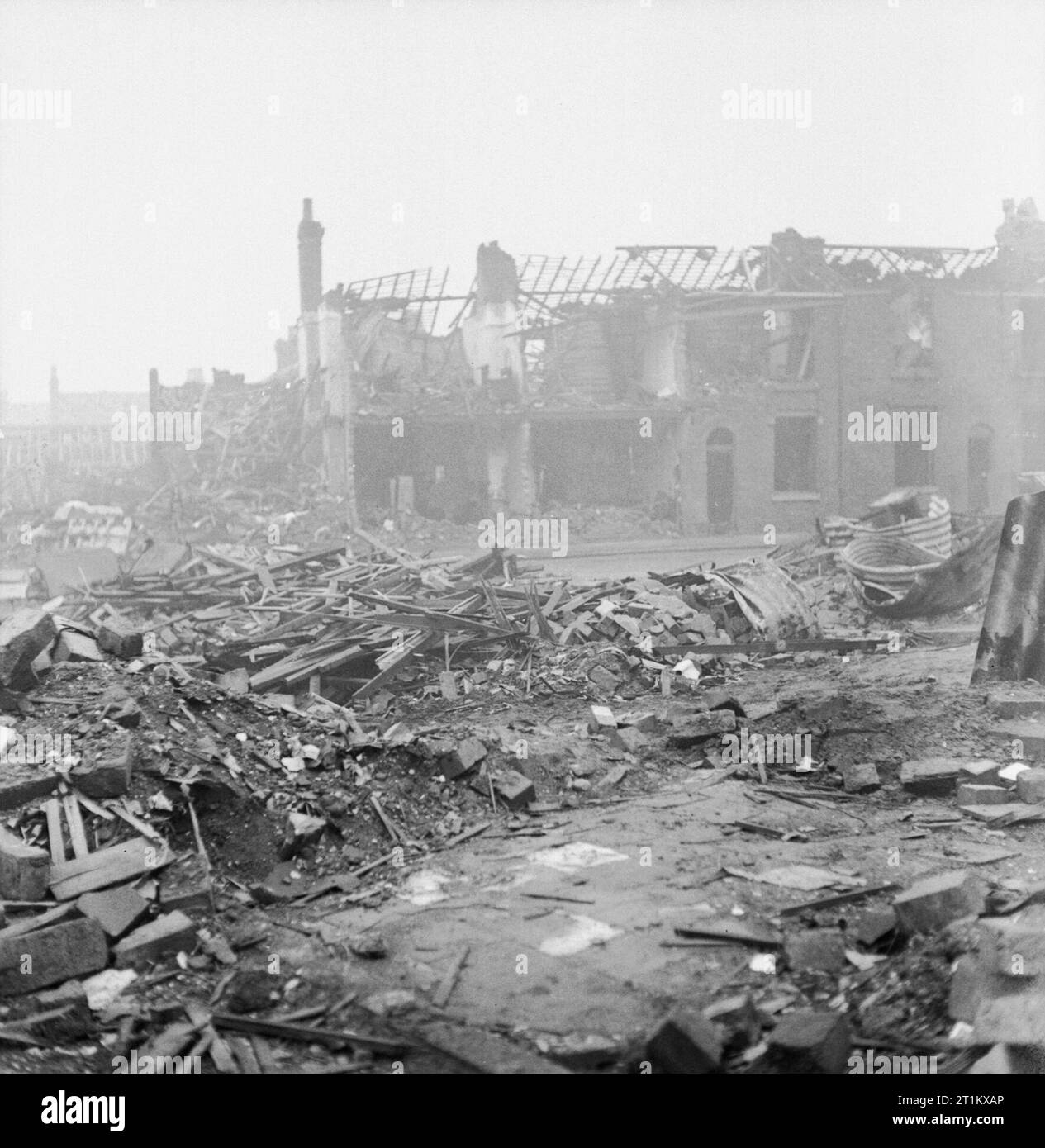 Bomb Damage in Birmingham, England, C 1940 Although some debris has been cleared on this site on James Street, Aston Newtown, Birmingham, a large pile of timbers and some brick rubble can be clearly seen. Also visible to the right of the photograph are the twisted remains of several Anderson shelters. In the background, two of the terraced houses that are still standing have had the front wall stripped away by the blast, revealing the interior walls and floors. Stock Photo