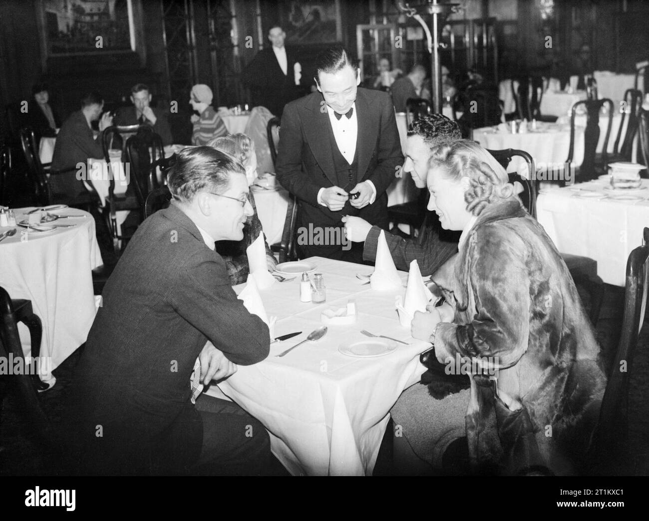 A group of diners give their order to the waiter at a restaurant in the West End of London, spring 1941. A group of four friends give their order to the waiter at this restaurant, somewhere in the West End of London. This restaurant is operating quite a luxurious service, with white table cloths and linen napkins visible on all the tables. Stock Photo