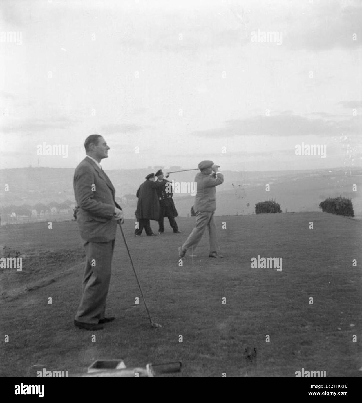 Brighton Today- Everyday Life in Wartime Brighton, Sussex, England, UK, 1944 A scene on the East Brighton golf course, which is perched on the Downs, overlooking the town. Playing his shot is the club's professional golfer, Charles Parsons, who has been with the club for 36 years. According to the original caption, he has been professional champion of Sussex five times and is the only man alive who has hit 18 holes in one. In the foreground is Charles Morris, the captain of the club, who is described in the original caption as 'shipbuilder, inventor and engineer, a well known Brighton sportsma Stock Photo