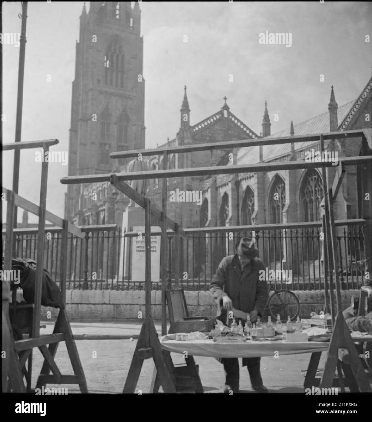 Boston Market- the Country Market and May Fair, Boston, Lincolnshire, England, UK, 1945 A man selling medicines arranges his wares on his stall in the marketplace at Boston, Lincolnshire. Directly behind him can be clearly seen 'Boston Stump', St Botolph's Church. On the church railings, a poster advertising a 'united service of thanksgiving' celebrating the 'cessation of hostilities' is just visible. Stock Photo