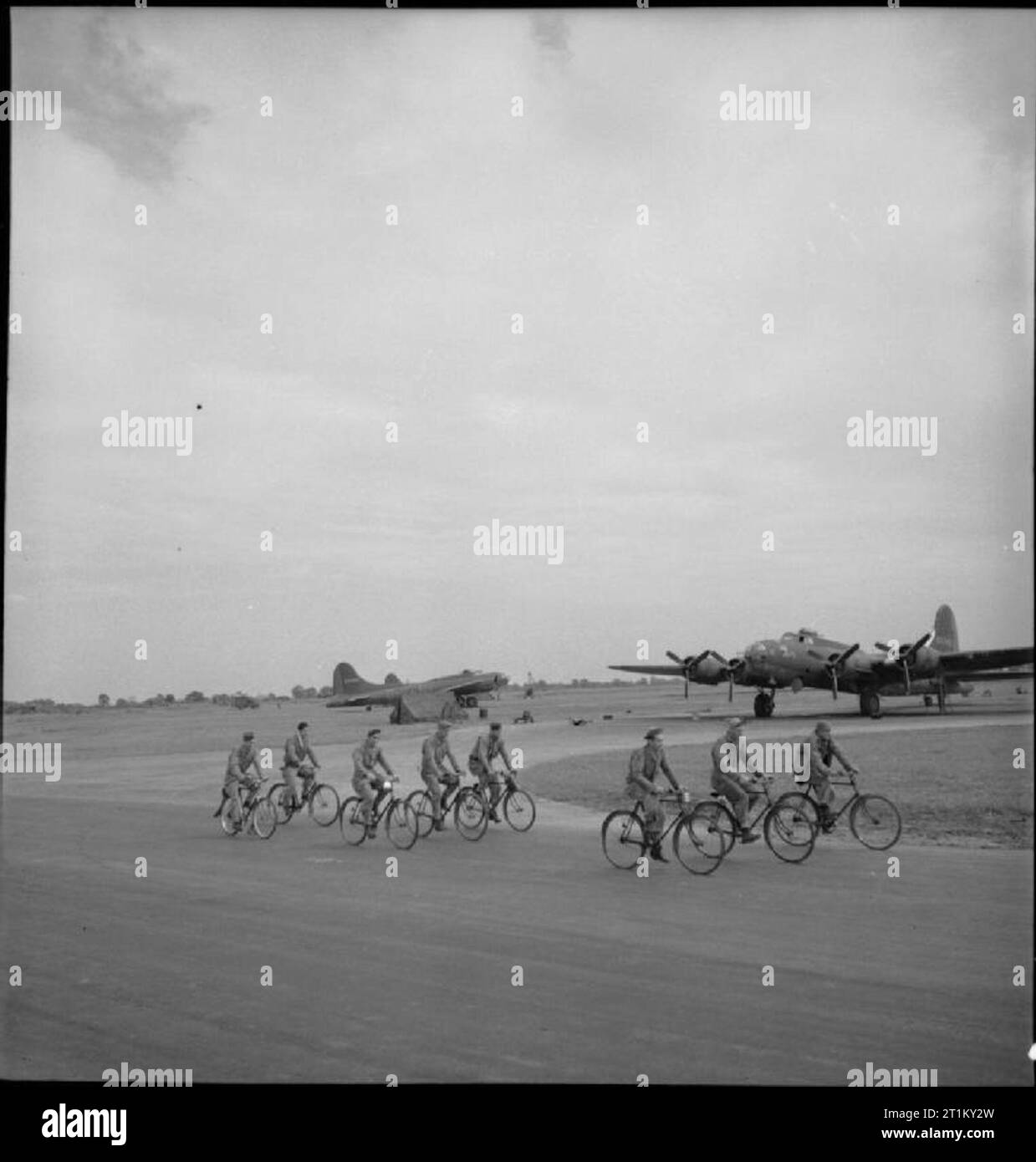 British Equipment at An American Airfield- Anglo-american Co-operation in Wartime Britain, 1943 A large group of bomb-dump staff at an American airfield somewhere in Britain ride bicycles past several aircraft on their way off-base. According to the original caption: 'vast numbers of bicycles are supplied to US Army Air Corps stations where restrictions on motor transport and big areas to be covered make their use essential'. The aircraft on the left features the letters NV, indicating that it is an aircraft of 326 Squadron, 92nd Bombardment Group. Stock Photo