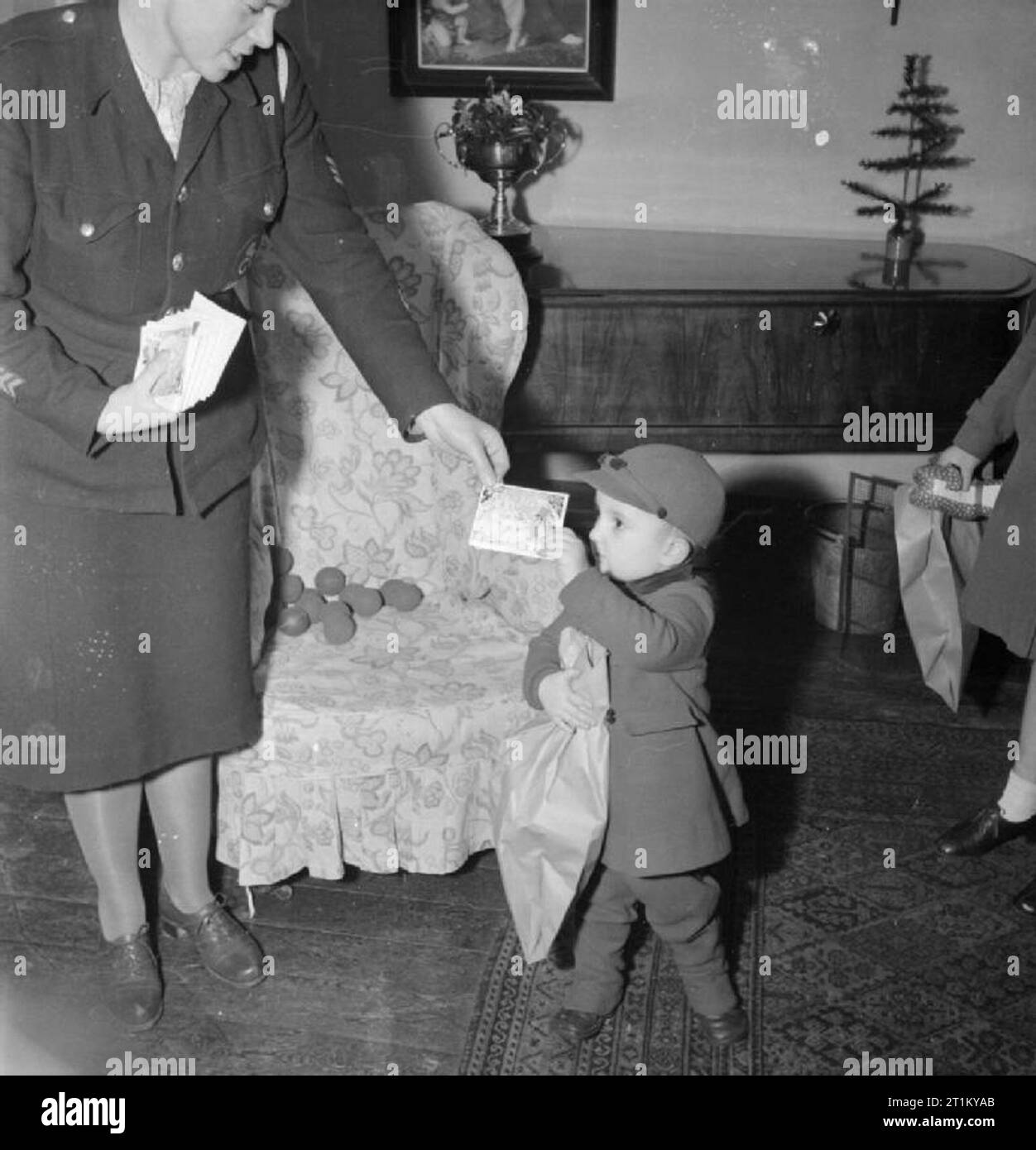 Bwrs Christmas Gifts Distributed To London's East Enders- American Aid To the Canning Town Settlement, London, England, UK, December 1944 At the Canning Town settlement, Derek Cunningham receives a Christmas card and savings stamp. In addition, he is holding a paper bag containing a new toy and some sweets, donated as Christmas gifts by America through the British War Relief Society. Stock Photo