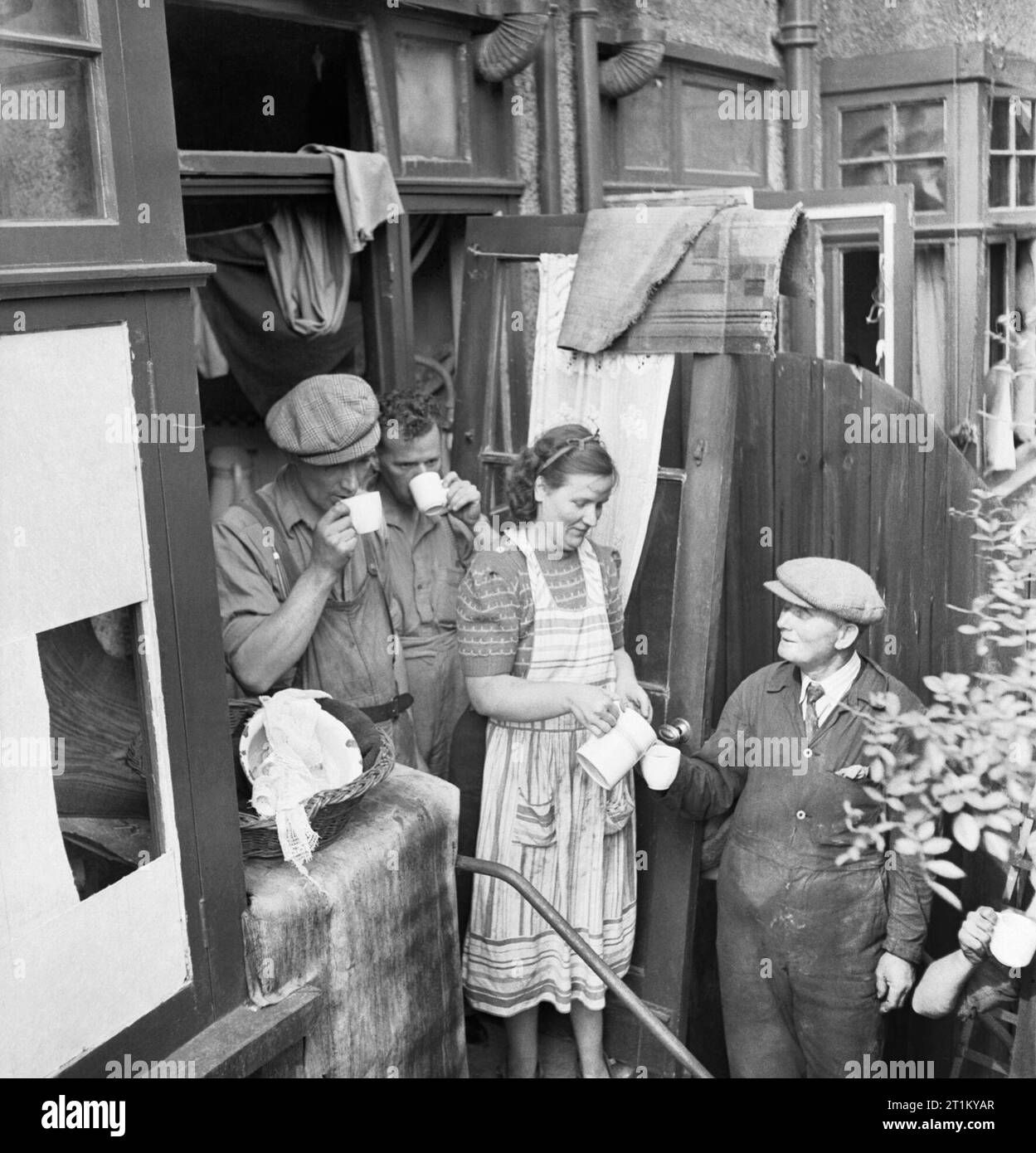 Builders are given cocoa as they make repairs to a house in London damaged by a V1 Flying Bomb in 1944. Mrs Calloghan gives cocoa to the team of builders who are repairing the damage to her London home following a V1 attack. The original caption states that she had just returned from evacuating her children to the country when the attack occurred and, although she has no windows and a damaged roof, she is not moving out of her home. The builders are part of the 'Blitz Repair Squad', a team of builders who have come to London from various parts of the country to help repair such damage. Stock Photo