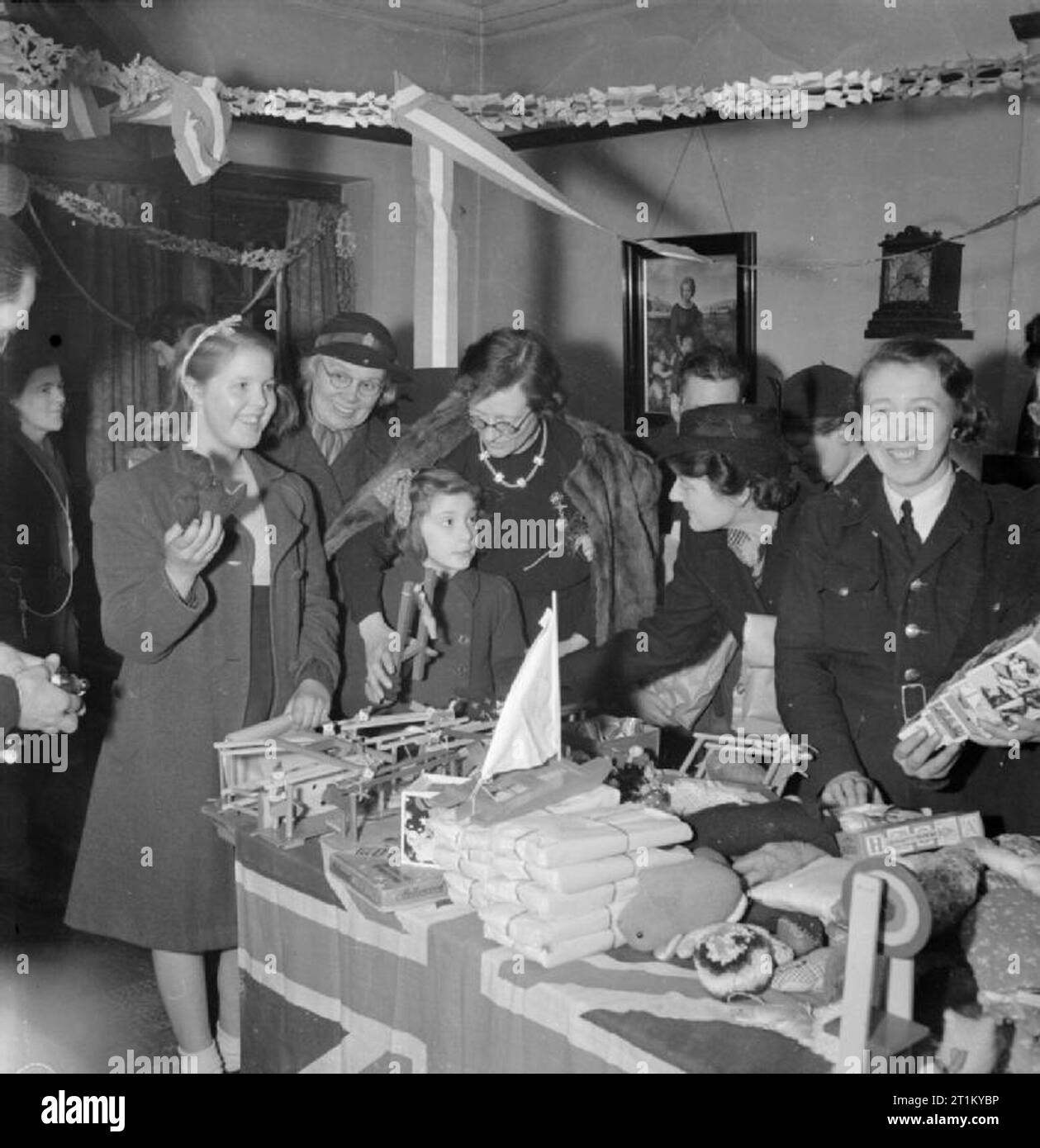 Bwrs Christmas Gifts Distributed To London's East Enders- American Aid To the Canning Town Settlement, London, England, UK, December 1944 Miss Constance Holland, the warden of Canning Town settlement, (centre) helps Norma Terry and Doreen Jones (left) to choose a gift from the pile of American toys on the table in front of them. The room is decorated with paper streamers and a member of the Women's Voluntary Service (WVS) can be seen between Doreen and Norma. The girls are both from Plaistow. Stock Photo