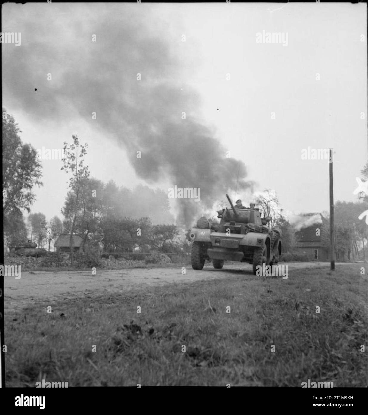 The British Army in North-west Europe 1944-45 A Daimler armoured car of 2nd Derbyshire Yeomanry, 51st Highland Division, passes a burning house in St Michielsgestel, during the drive on Hertogenbosch, 24 October 1944. Stock Photo