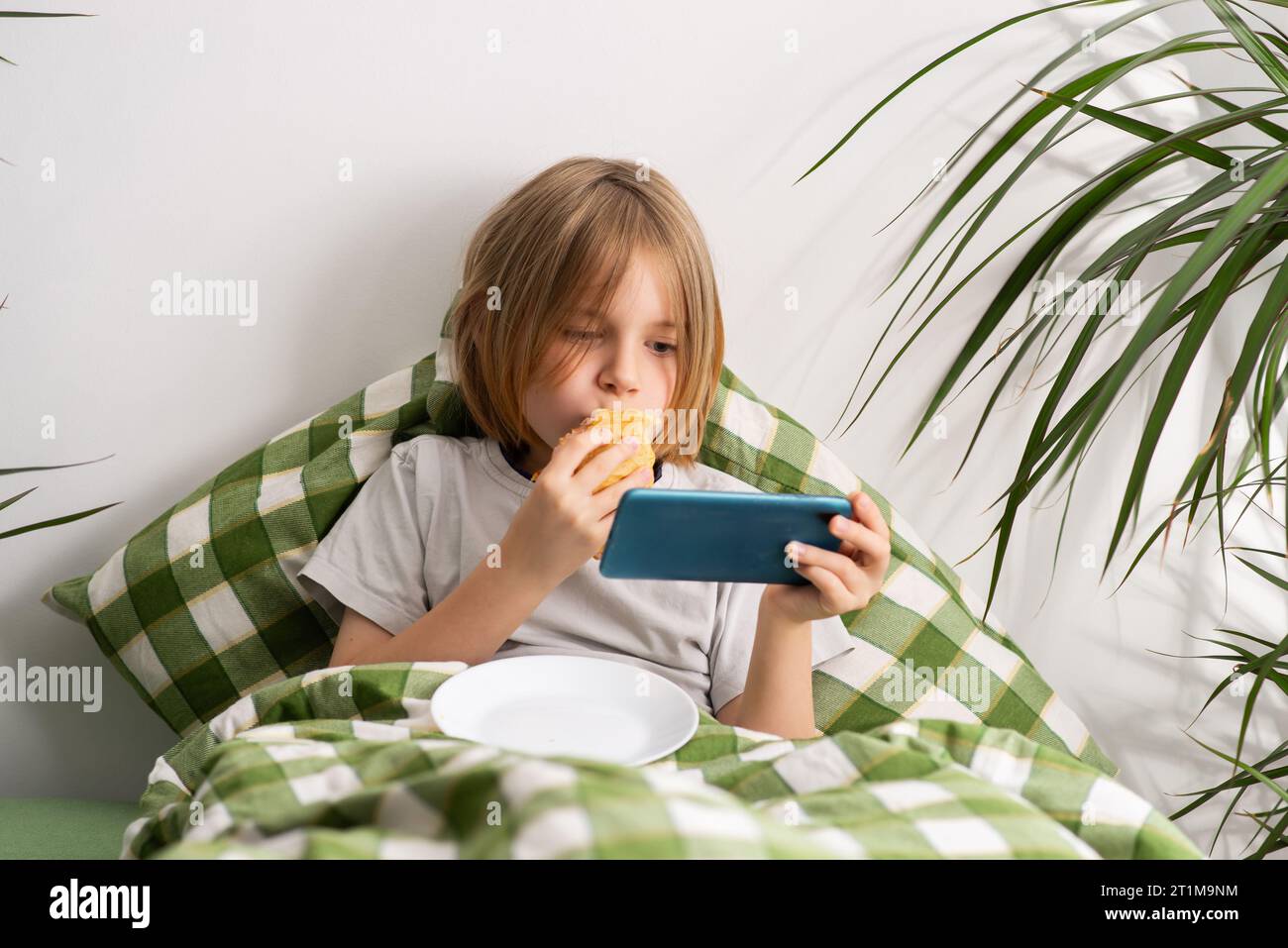 In the bed, a 9-10-year-old boy with flowing locks enjoys a toast ...
