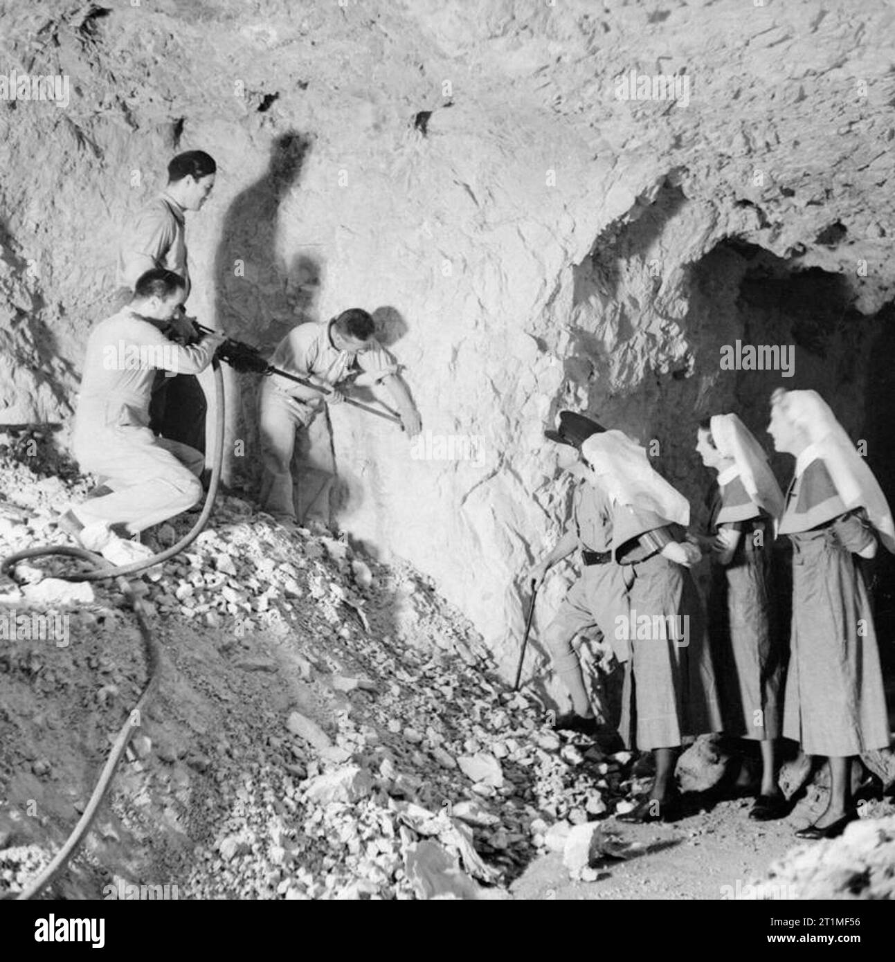 In a Gibralter Underground Hospital When most of the civilian population of Gibralter was evacuated, a hospital was established in one of the air raid shelters cut into the solid rock. It is constantly being added to and is ready for any eventuality. The work of excavation is being done by Civilian engineers, leaving the Royal Engineers to concentrate on defence works. This image shows skilled civilian workmen of the new City Council's staff engaged in construction of a new ward of the hospital. Officer Commanding Hospital and Nursing Staff look on. Stock Photo