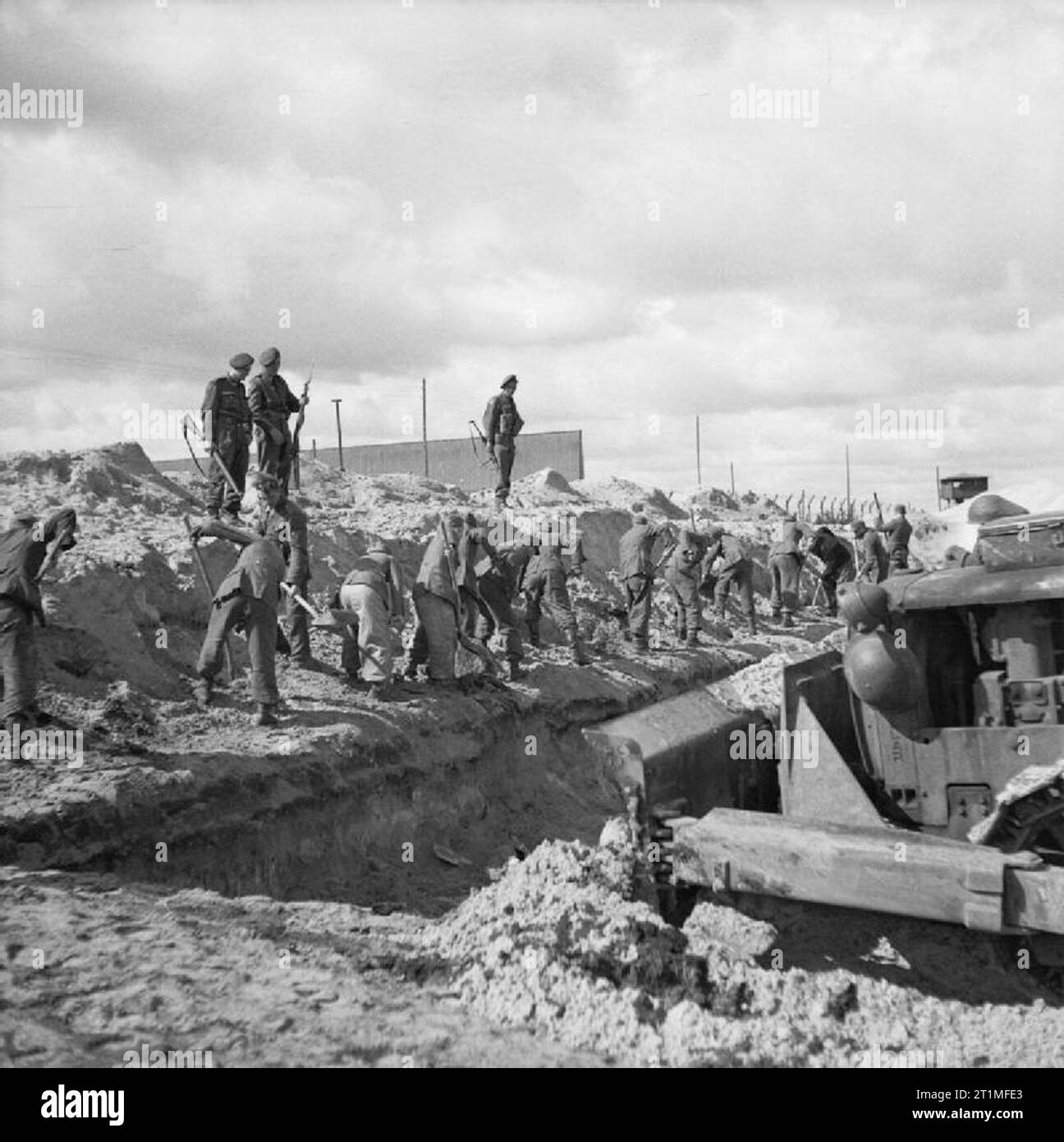 The Liberation of Bergen-belsen Concentration Camp, April 1945 German SS guards and a bulldozer fill in a mass grave. Stock Photo