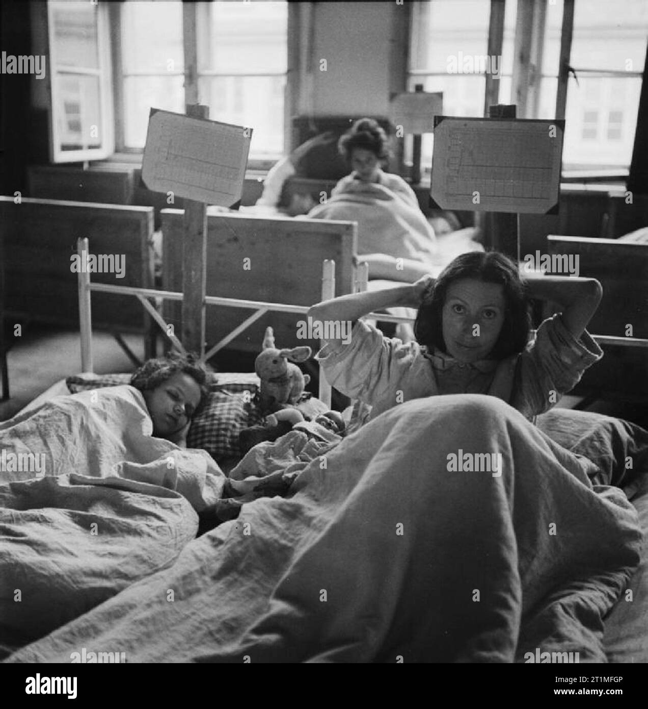 The Liberation of Bergen-belsen Concentration Camp A woman inmate combs her hair while lying in bed in one of the wards at the hospital set up in Hohne Military Barracks nearby. Her child sleeps beside her with a toy on her pillow provided by the British Red Cross. Stock Photo