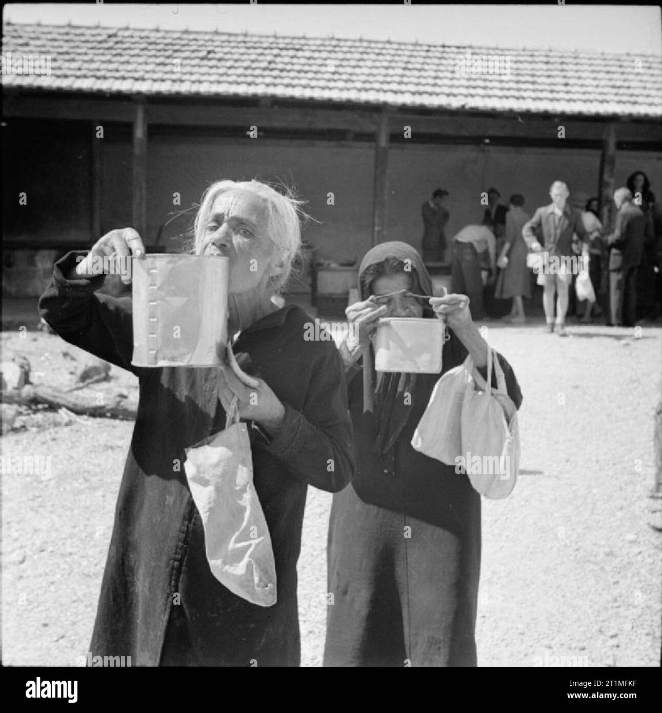 The Liberation of Rhodes, 1945 Two elderly Greek women sip their soup as they leave a Red Cross kitchen. They also carry bags so that they can call at a food distribution centre to collect their rations. During the German occupation the local inhabitants had suffered the effects of malnutrition due to insufficient food. After the liberation of the island the British quickly began to organize food supplies, issuing people with ration books and distributing essential food stuffs. Red Cross kitchens also assisted by providing nourishing soup. Stock Photo