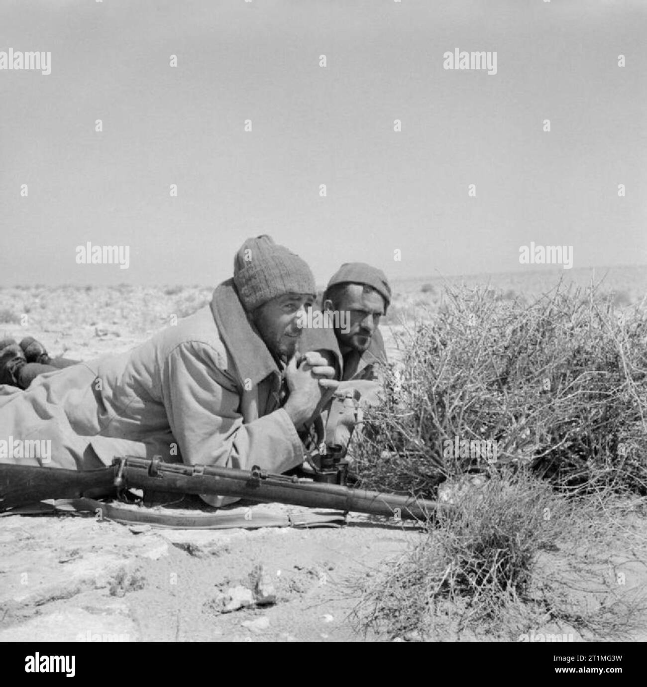 Two men of an LRDG (Long Range Desert Group) patrol on a road watch in North Africa, 25 May 1942. Two men of a Long Range Desert Group patrol, dressed in greatcoats, make use of available cover while on a road watch. Stock Photo