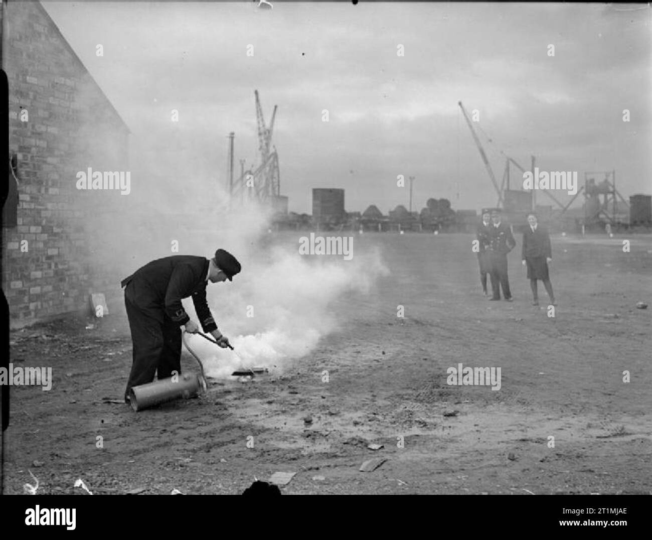 The Dockyard Cinema Maintenance Unit, Rosyth, Scotland, January 1944 In an empty part of the dockyard, Lieutenant Commander K Porter, CCMO, of the Dockyard Cinema Maintenance Unit in Rosyth shows two WRNS and a naval officer, who stand at a safe distance, how to tackle a burning reel of nitrate film with a fire extinguisher. Stock Photo