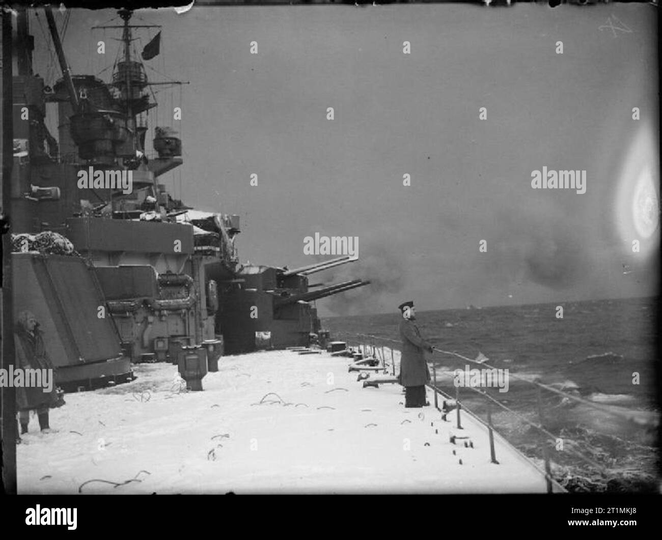 The Royal Navy during the Second World War The snow covered decks of HMS KING GEORGE V on Northern convoy duty. Often the decks were a foot deep in snow. Two of the ships 5.25 inch gun turrets can be seen beyond the sailor looking out to sea. Stock Photo