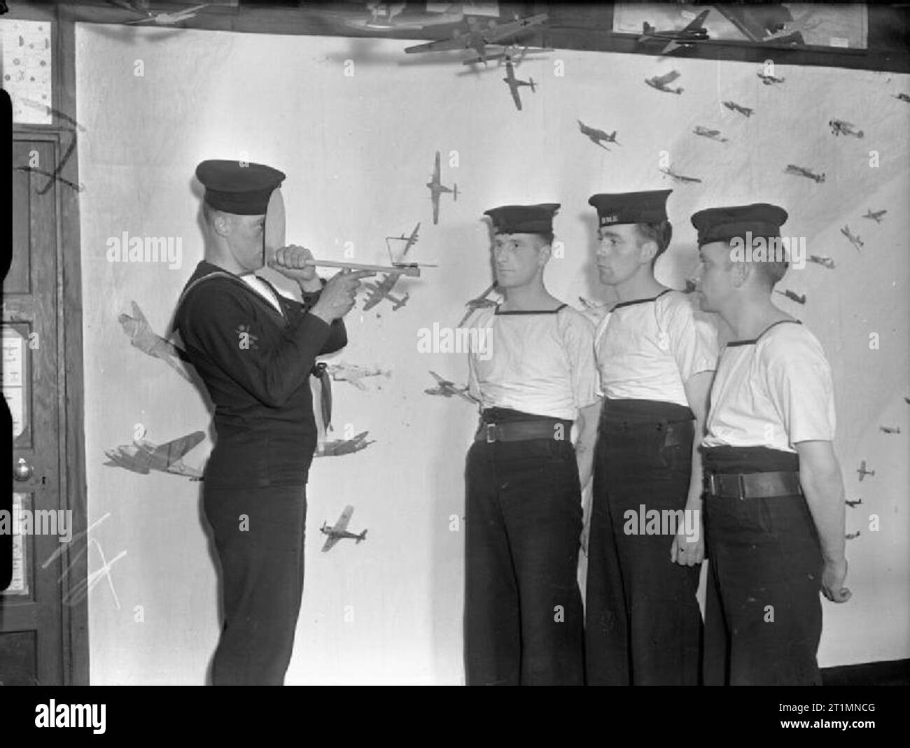 The Royal Navy during the Second World War Four Royal Navy Ratings take part in a gunnery and aircraft recognition class using a visual trainer to assess the bearing and angle of an aircraft. Behind them is a collage of illustrations of aircraft in different positions angles and bearings etc. Stock Photo
