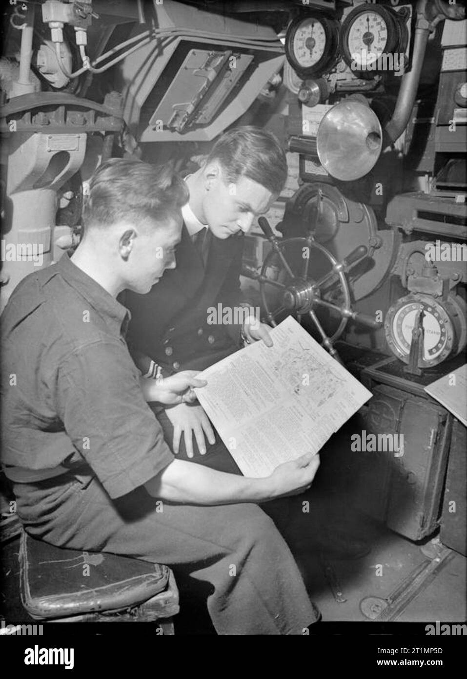 The Royal Navy during the Second World War Scene on board HMSM STORM at Portsmouth with Telegraphist S Staines of Hapden Park, Eastbourne, and the Commanding Officer, Lieutenant Commander E P Young, DSO, DSC, RNVR, of Enfield, looking at their Christmas 1944 'Good Evening' programme and sketch designed by Staines. Lieutenant Commander Young was the first RNVR officer to command an operational submarine in the war. Stock Photo