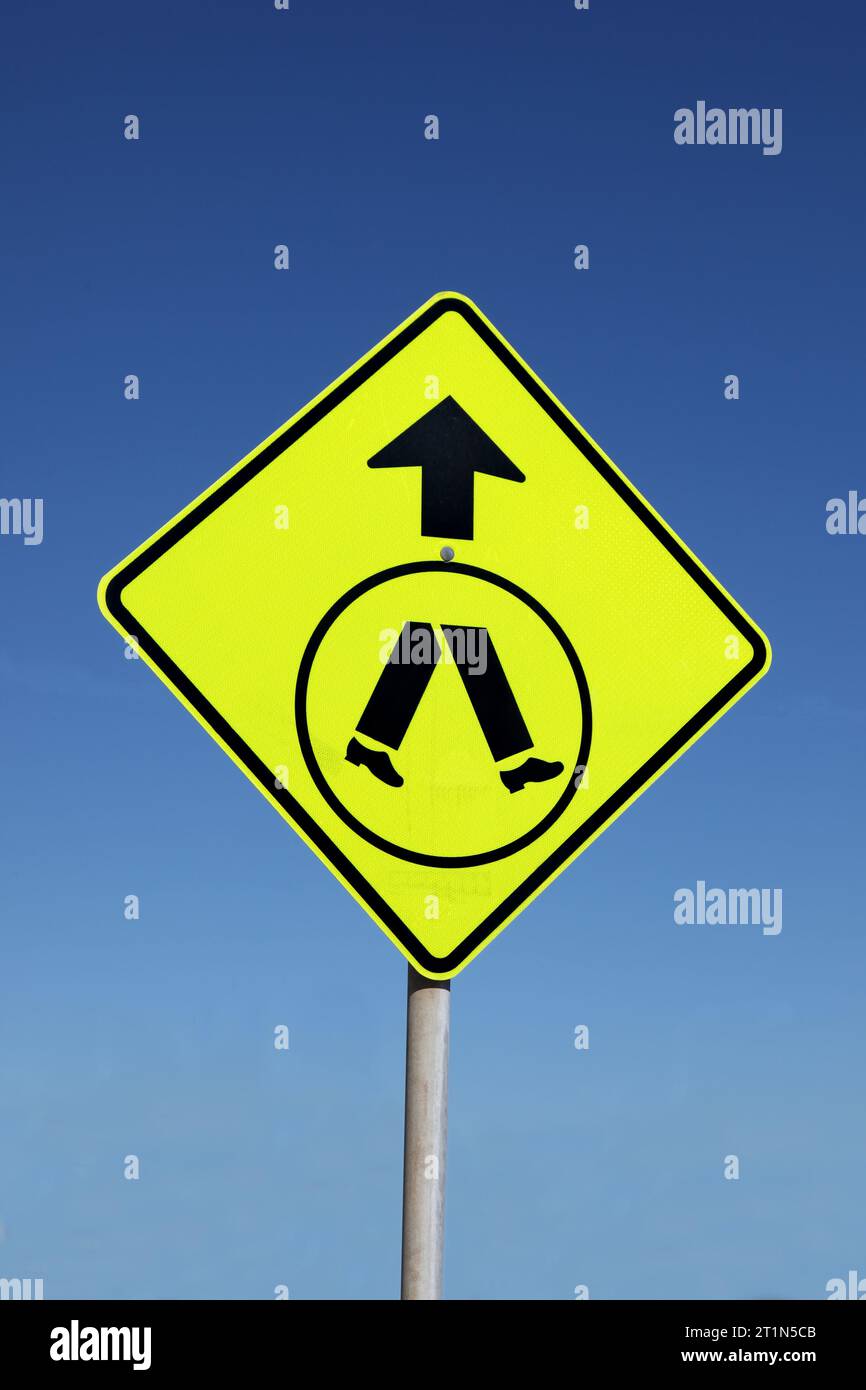 A bright yellow pedestrian crossing sign on blue sky background. Stock Photo