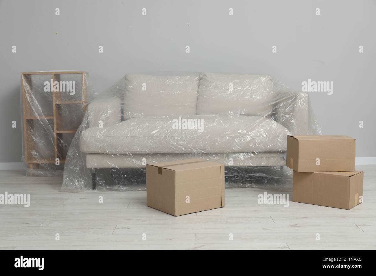 Shelving unit, sofa covered with plastic film and boxes near light grey wall indoors Stock Photo
