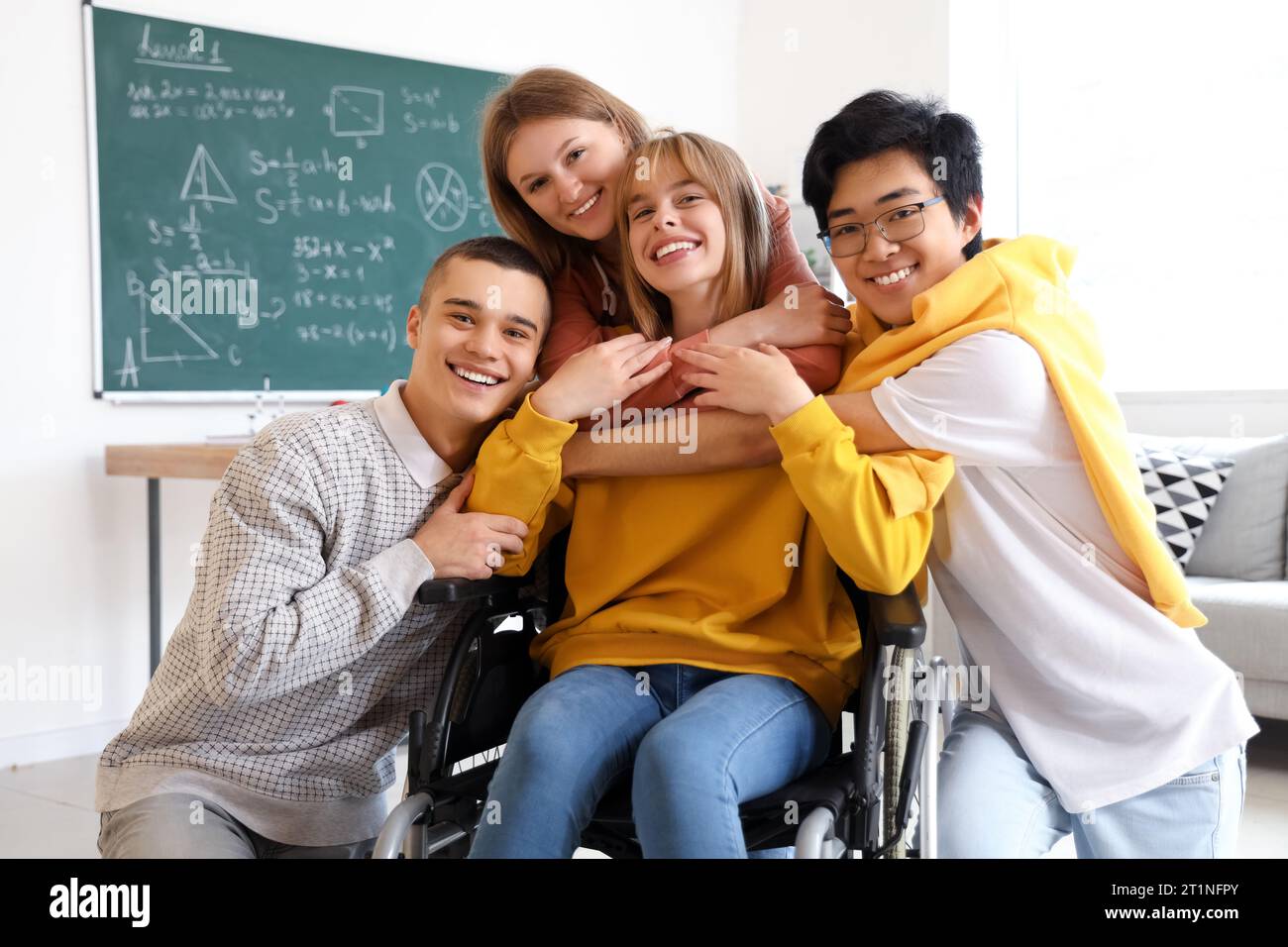 Group of teenage students with girl in wheelchair hugging at school ...