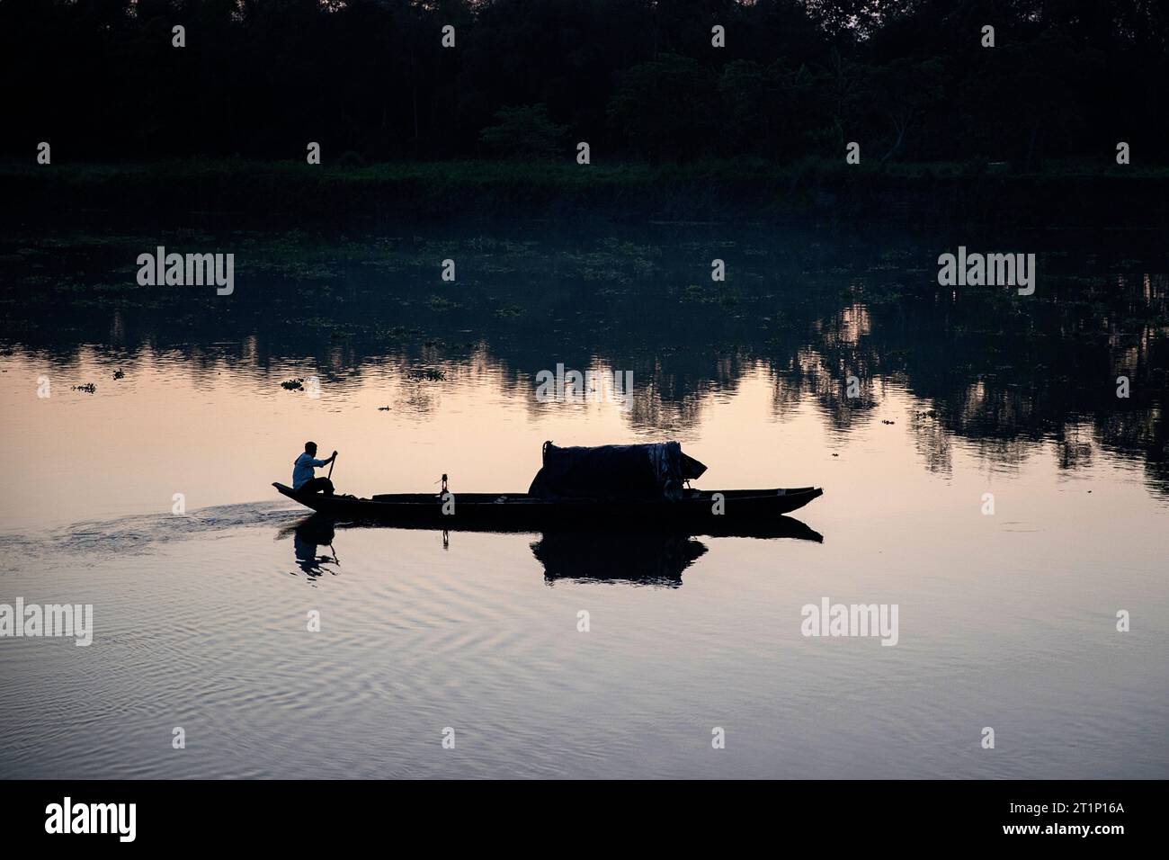 Silhouette of a local fisherman sitting on back of dugout canoe with light and rowing on river at sunset on Majuli Island, Assam, India Stock Photo