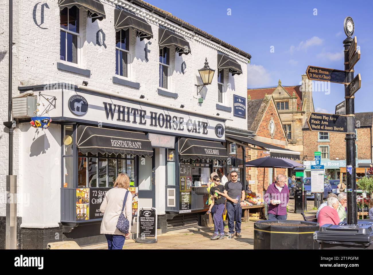 A street scene outside a whitewashed cafe in a market town. There is a signpost in the foreground and clear sky is above. Stock Photo