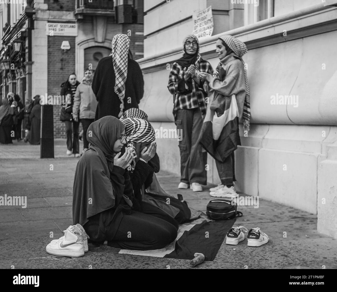 Black and white image of young arabic girls taking time out to pray at Pro Palestinian march in London. Stock Photo