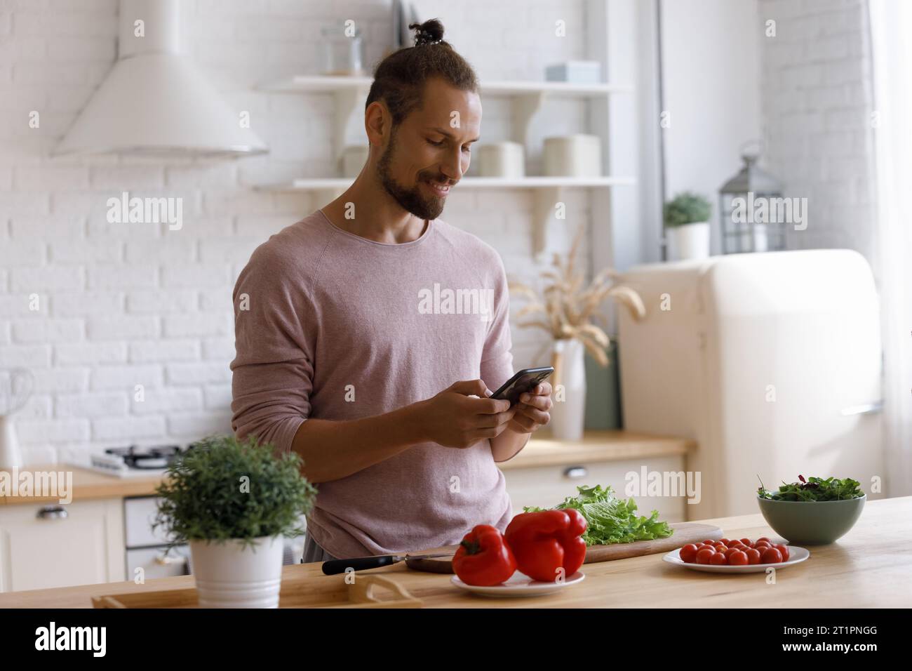 Positive young homeowner man using smartphone in kitchen Stock Photo