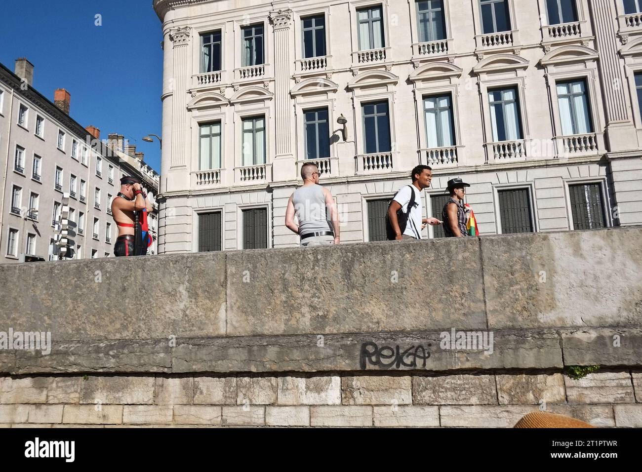 Four men walking on the river embankment in Lyon, France after a PRIDE march. Old buildings, sunny day, clearly gay men Stock Photo