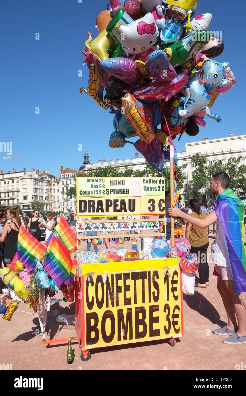 A vendor with a pole of of novelty balloons for sale at a PRIDE march & party in Pl. Bellecour, on a sunny day in Lyon, France Stock Photo