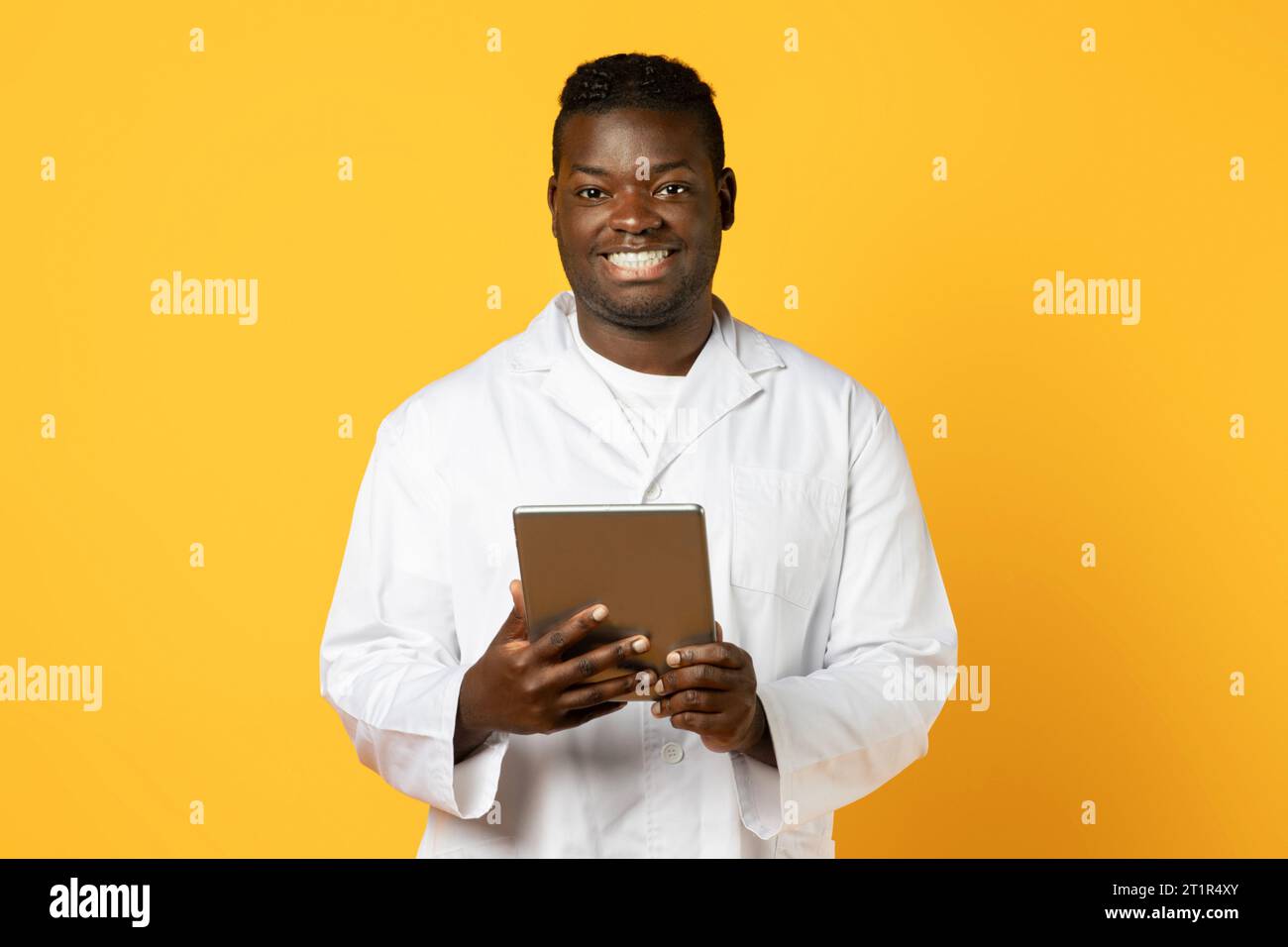 Cheerful black doctor man with tablet computer on yellow background Stock Photo