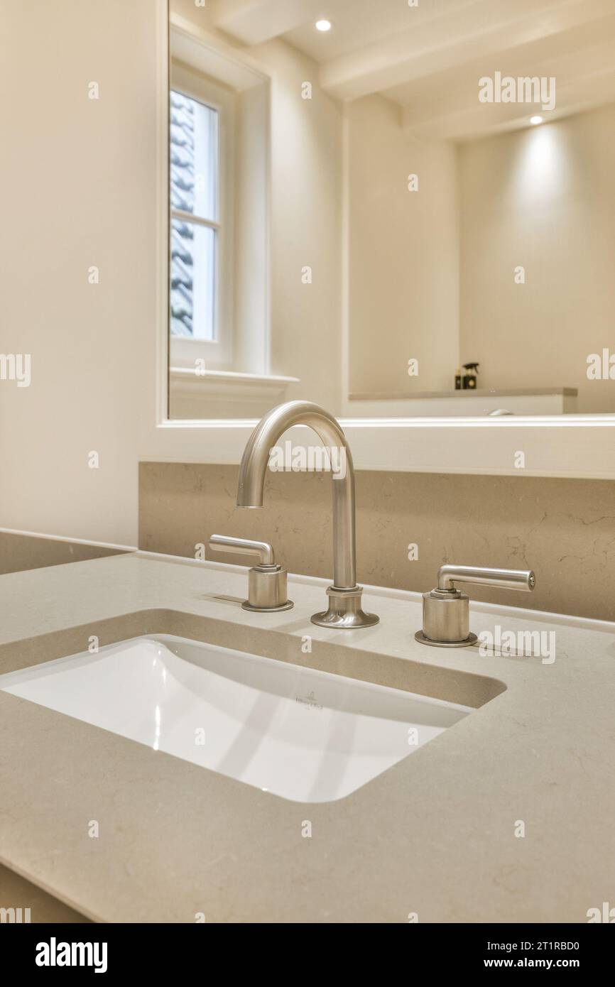 a bathroom sink with two faucets on the counter and an open window in the wall is behind it Stock Photo