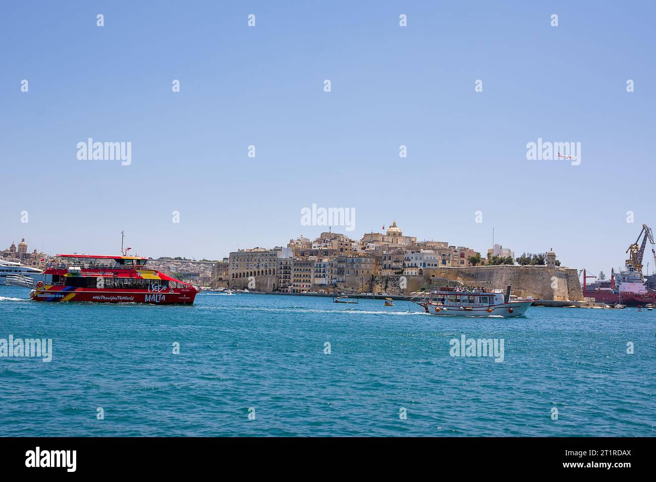 Valletta, Malta - 17 June 2023: Gulf between Valletta and Vittoriosa with passing boat with tourists and international plane in the sky Stock Photo