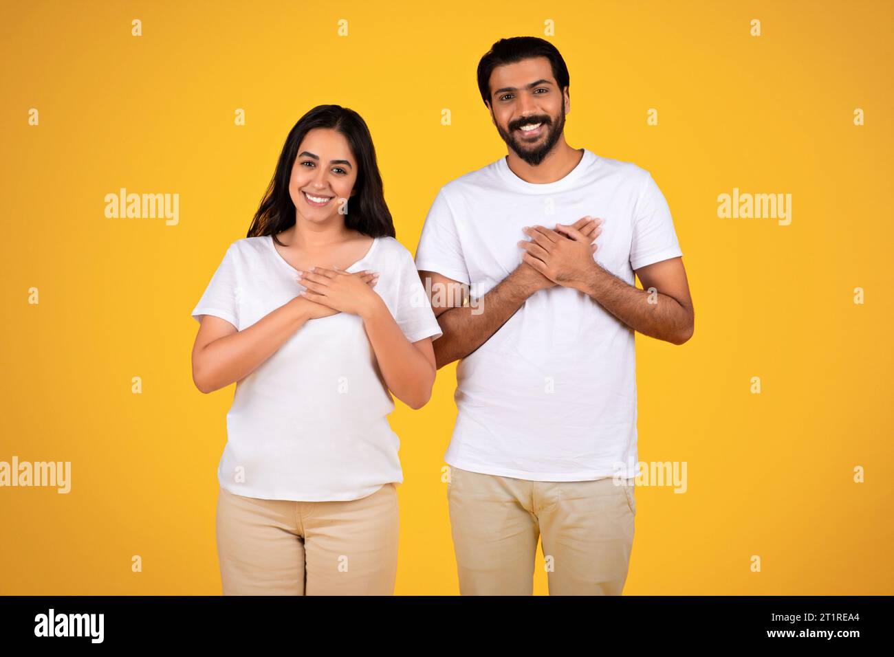 Couple placing hands on heart, yellow background Stock Photo