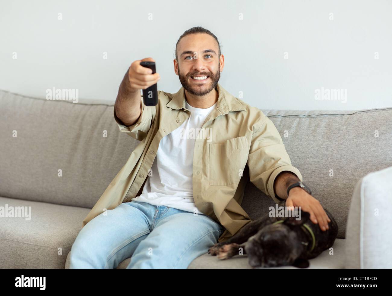 Happy millennial man having rest, switching channels with remote controller Stock Photo