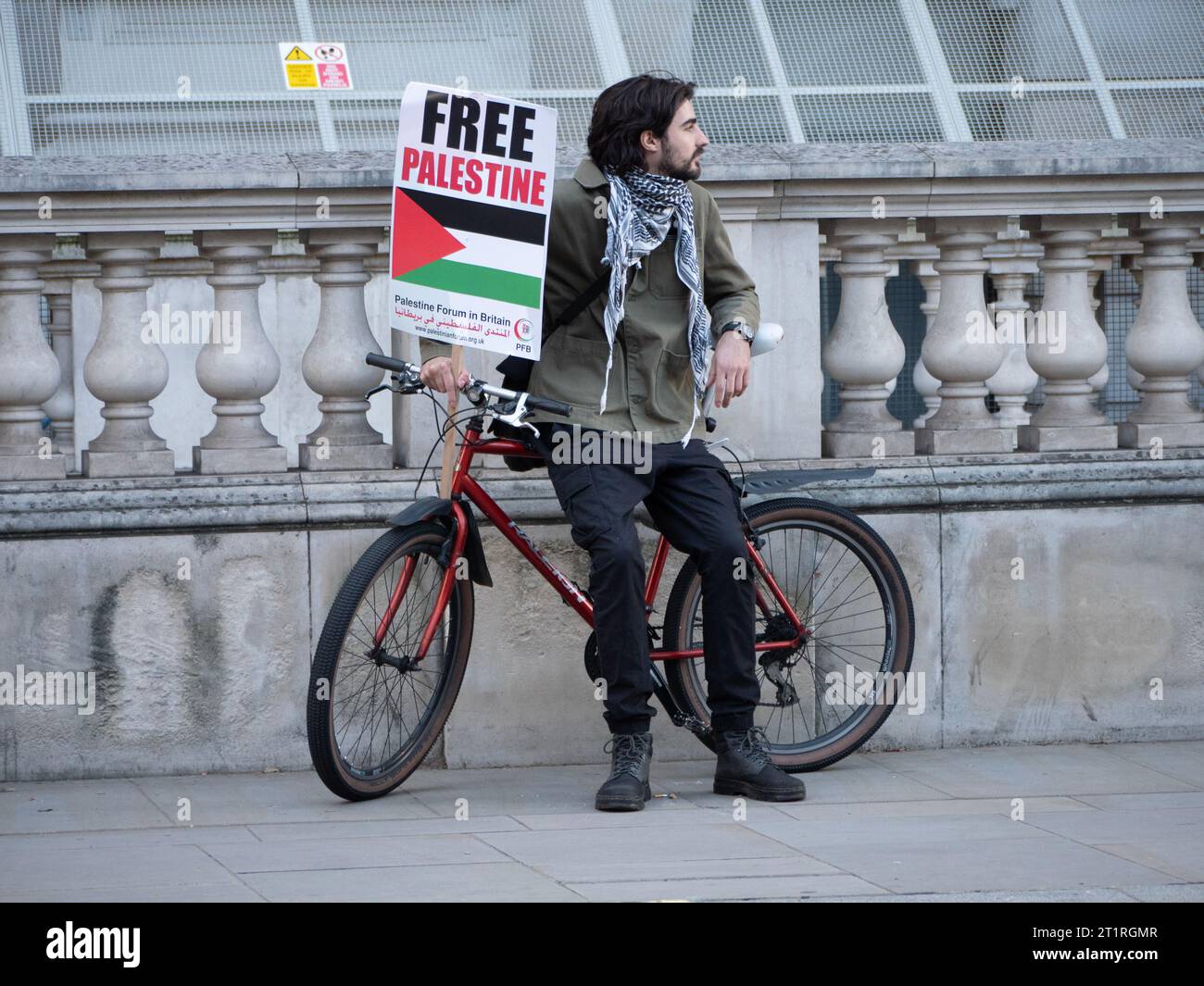 Pro-Palestinian marchers with Free Palestine poster sitting on bike  in Westminster London, UK, at the Palestine Solidarity Campaign demonstration, march to protest about the Israel Palestine confict over the Gaza Strip Stock Photo