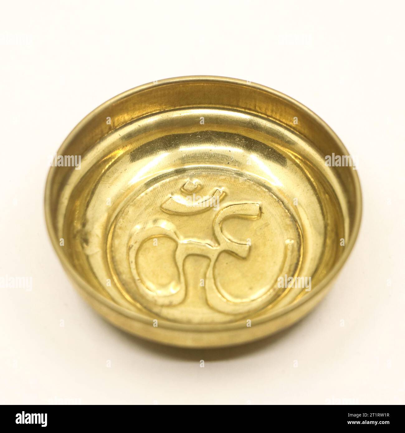 a traditional golden prayer bowl with an antique hindu om symbol carved inside the plate isolated in a white background Stock Photo
