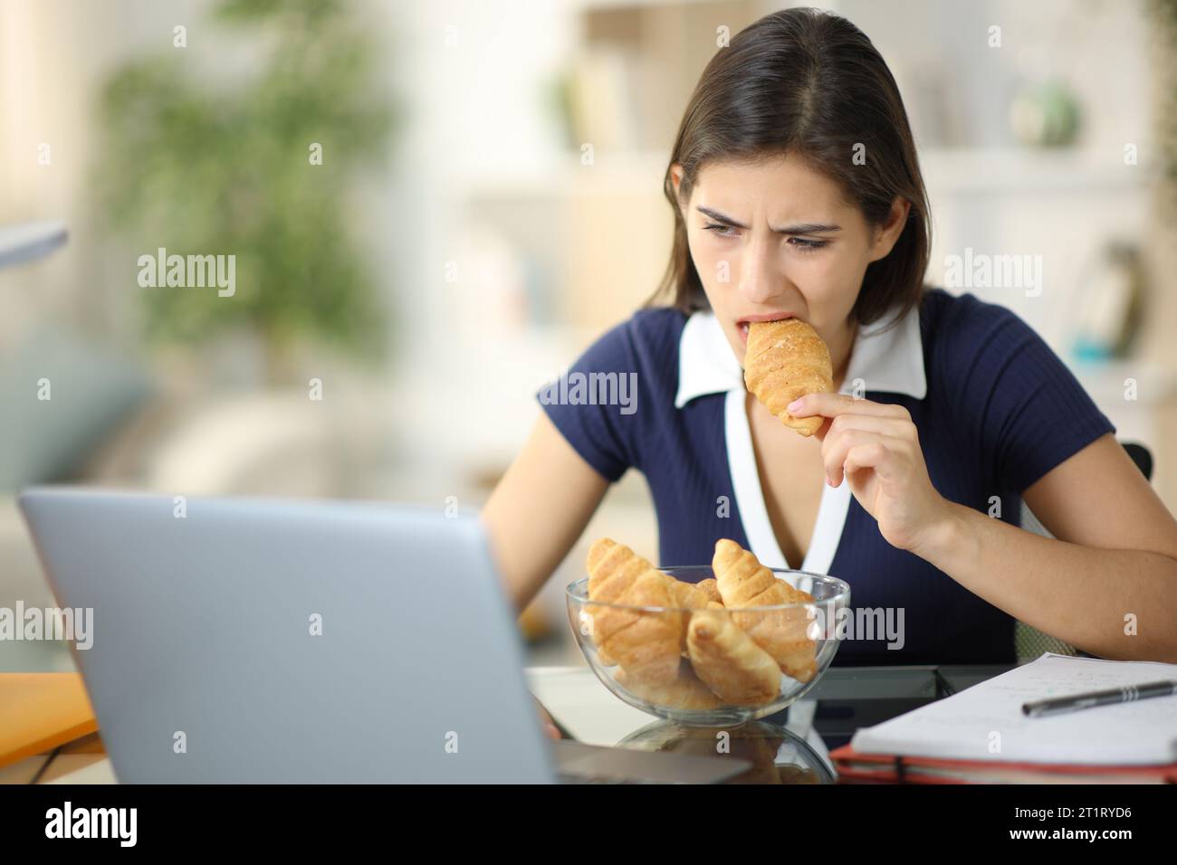 Glutton anxious student eating and studying online at home Stock Photo