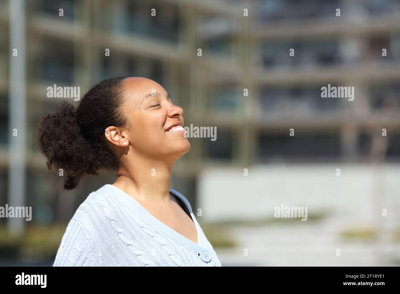 Happy black woman breathing fresh air standing in the street Stock Photo
