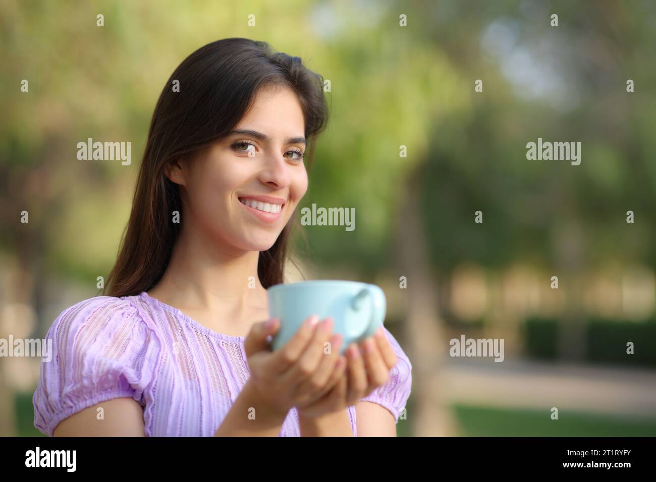 Happy woman looking at camera holding coffee cup in a park Stock Photo