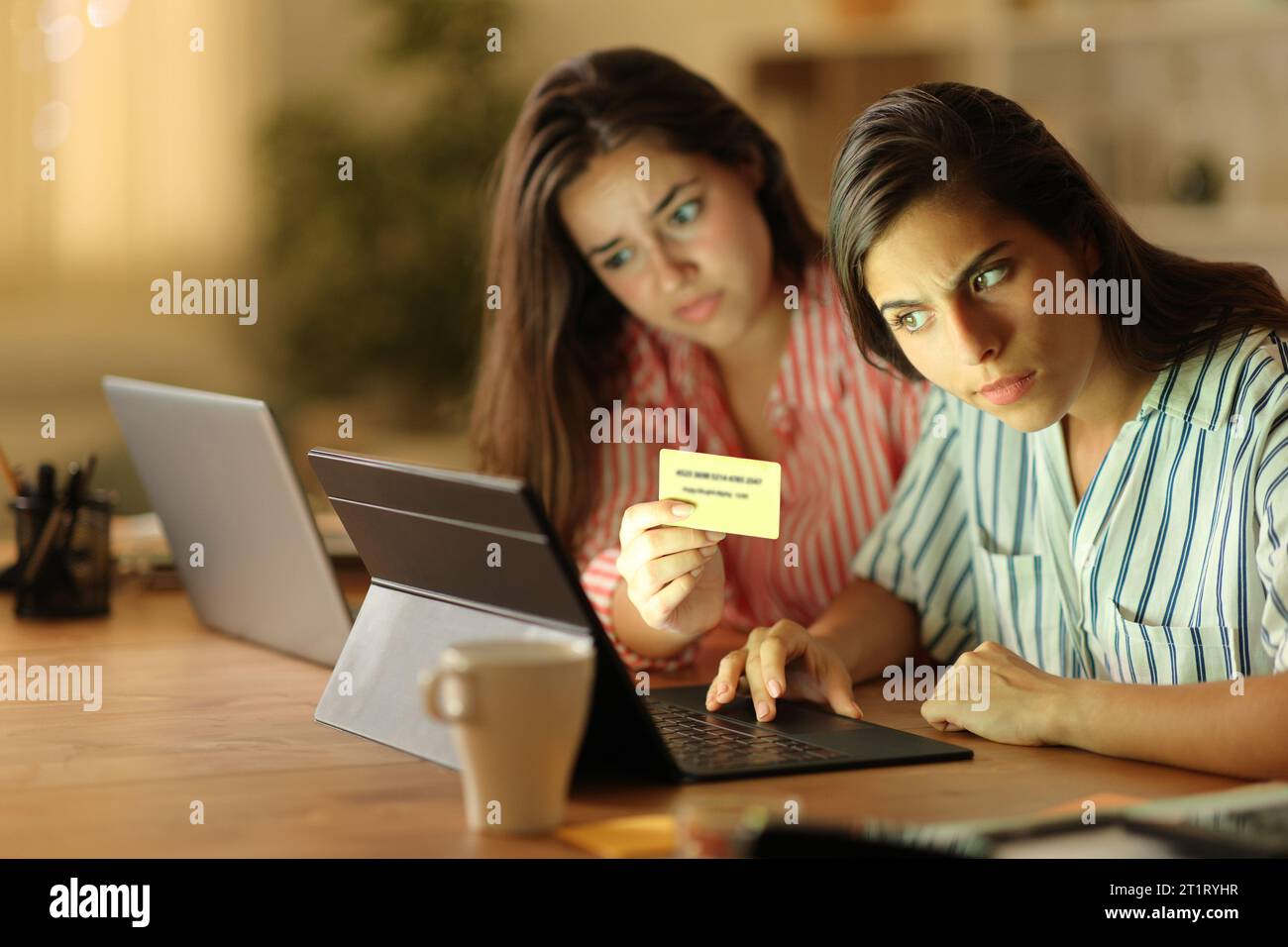 Two suspicious tele workers buying online with credit card and laptops in the night at home Stock Photo