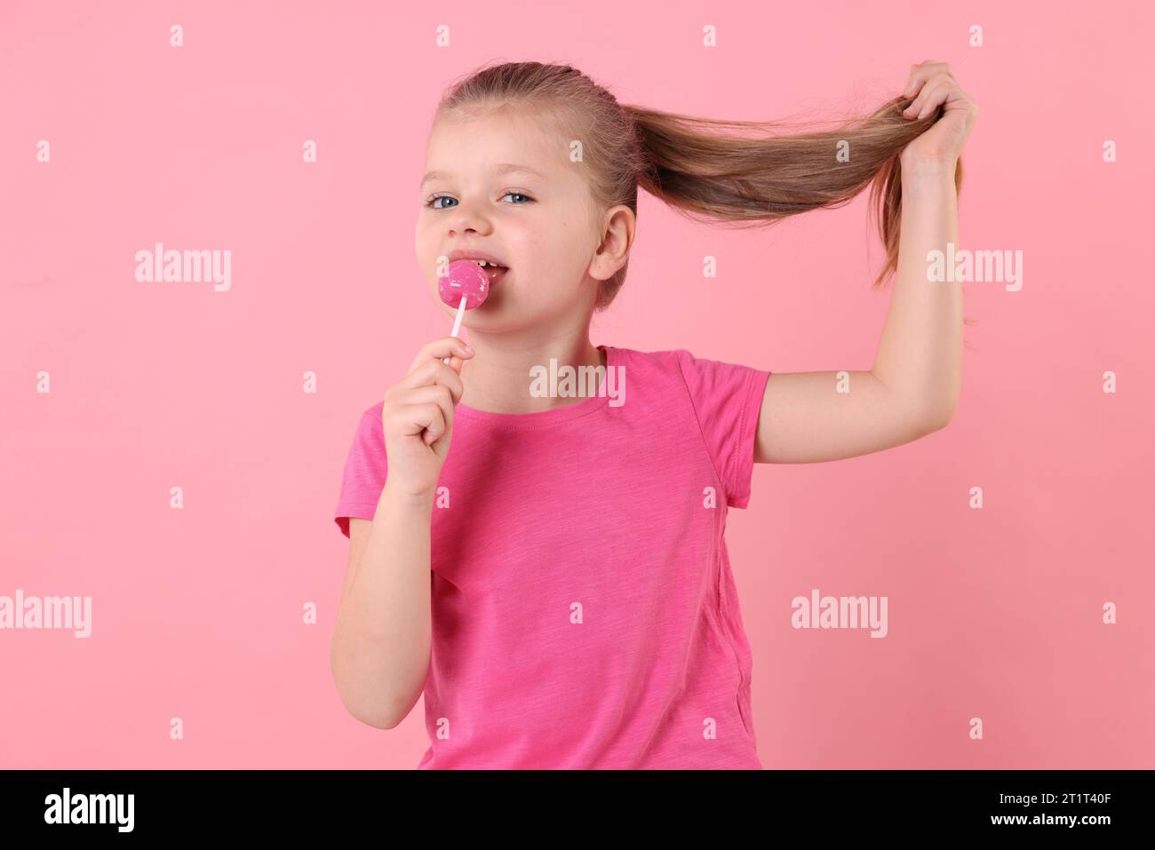 Cute little girl licking lollipop on pink background Stock Photo