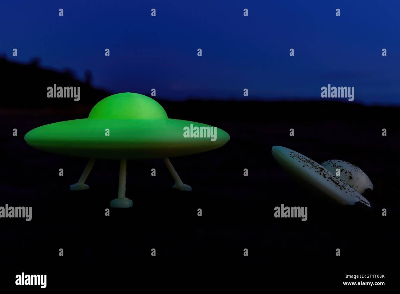 A glowing flying sauce stands next to a dark crashed UFO at night. Intentionally low quality photo to simulate a hoax photo taken with a cell phone. Stock Photo