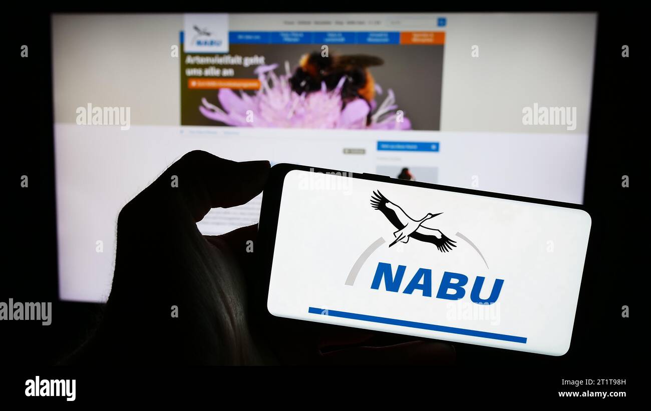 Person holding mobile phone with logo of association Naturschutzbund Deutschland e.V. (NABU) in front of web page. Focus on phone display. Stock Photo