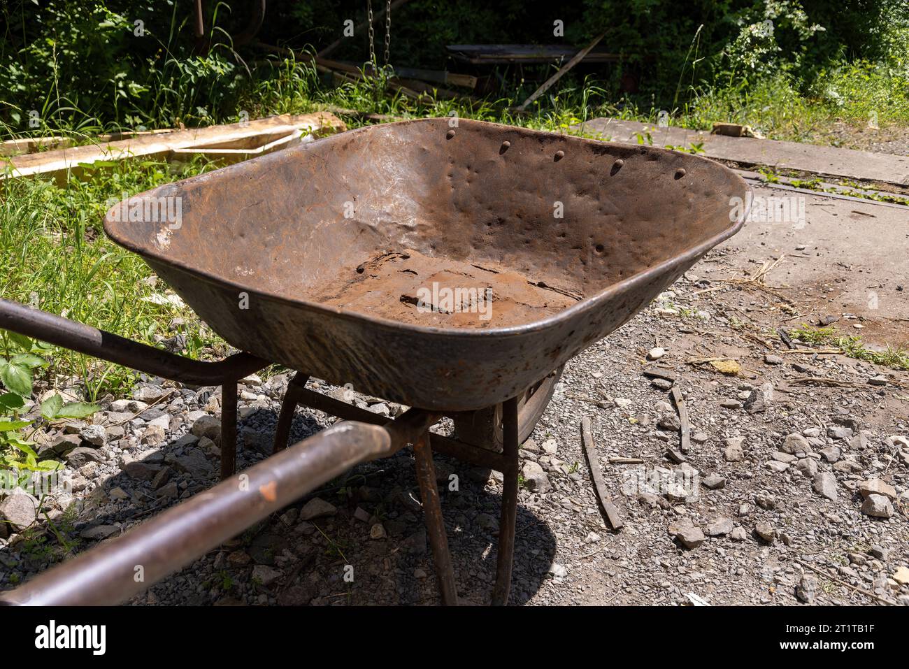 old, brown, rusted iron wheelbarrow with dents and holes Stock Photo