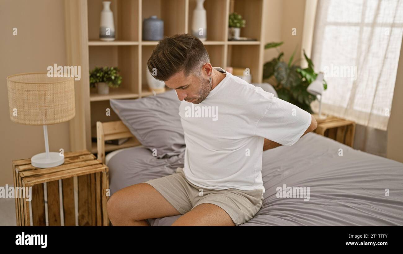 Worried, young hispanic man suffering from an agonizing back injury ...