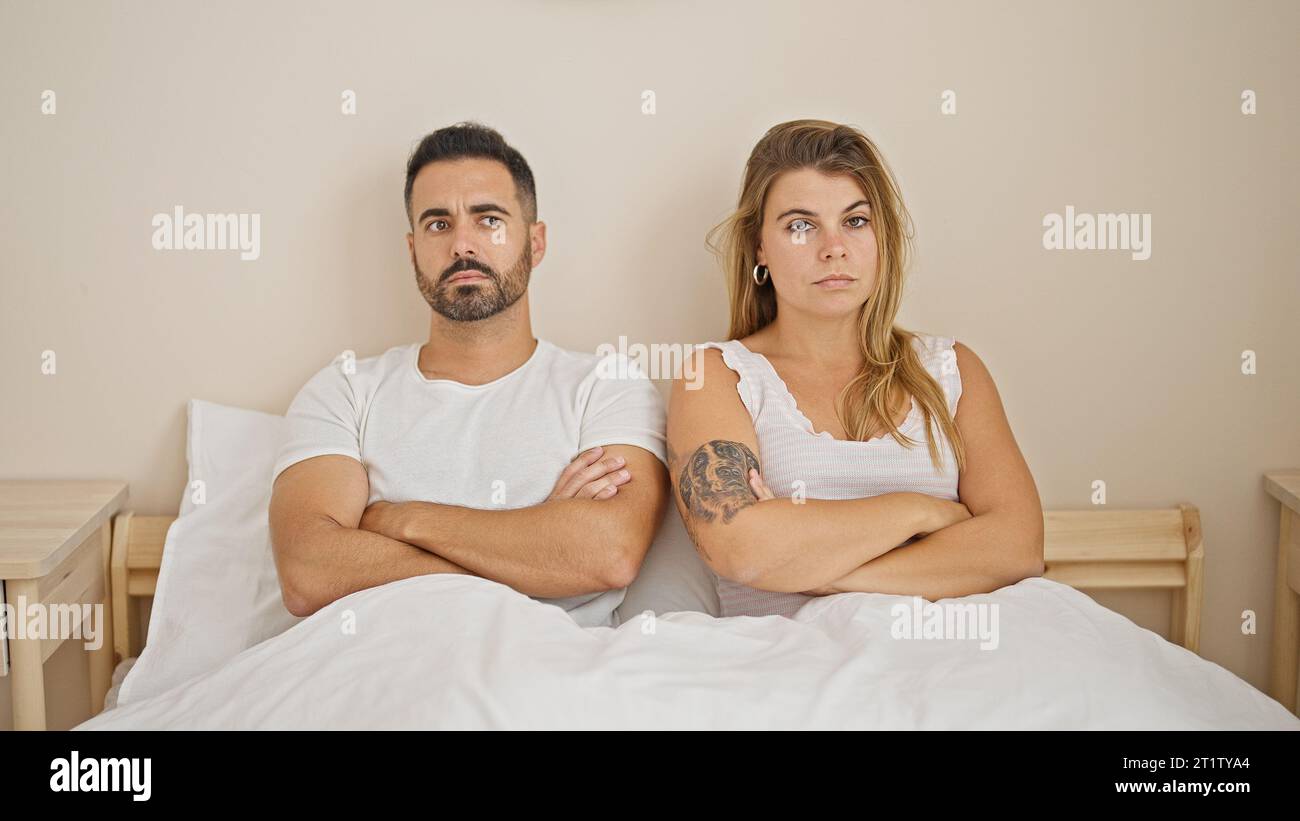 Man and woman couple sitting on bed with arms crossed gesture angry at ...