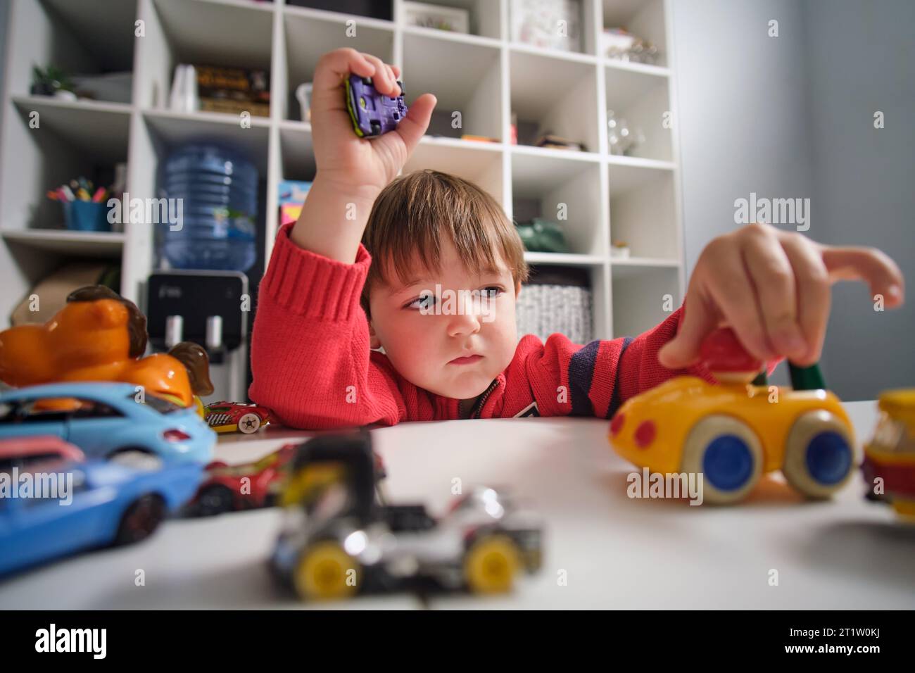 The happy baby spends his leisure time playing with toy cars at home ...