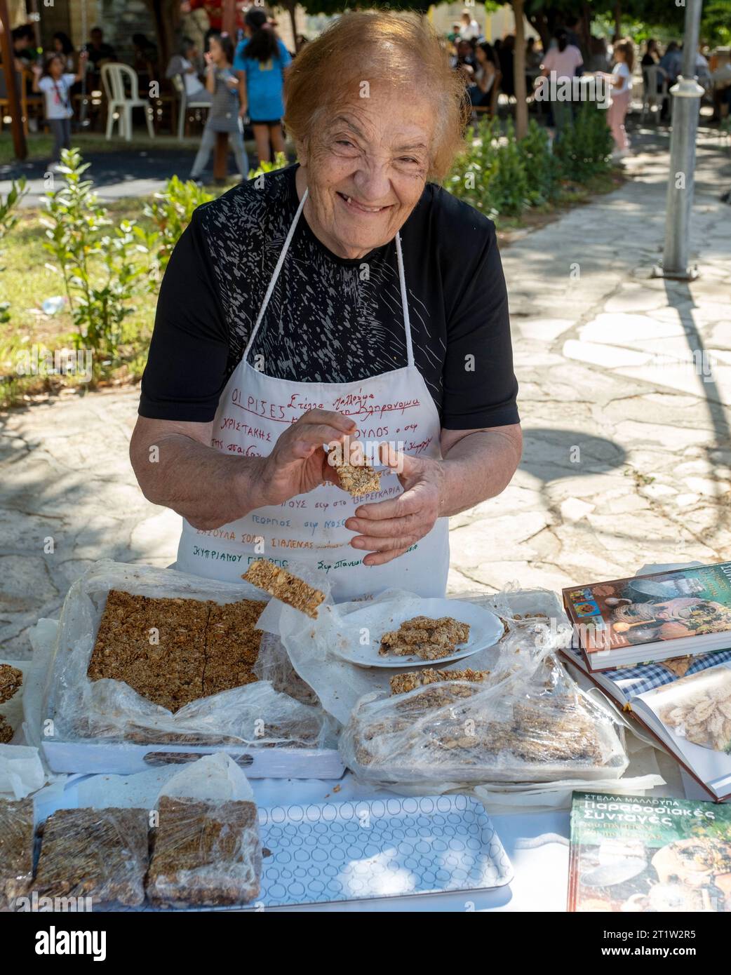 A senior lady selling  Pasteli bars made from nuts and honey at the Amargeti Olive Festival, Cyprus. Pasteli is a traditional Cypriot sweet bar. Stock Photo