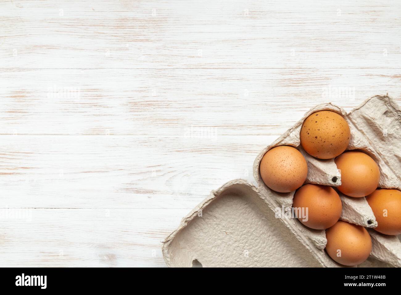 Brown eggs in open carton box on wooden background. Fresh organic chicken eggs in carton pack. Top view with copy space. Natural healthy food and orga Stock Photo