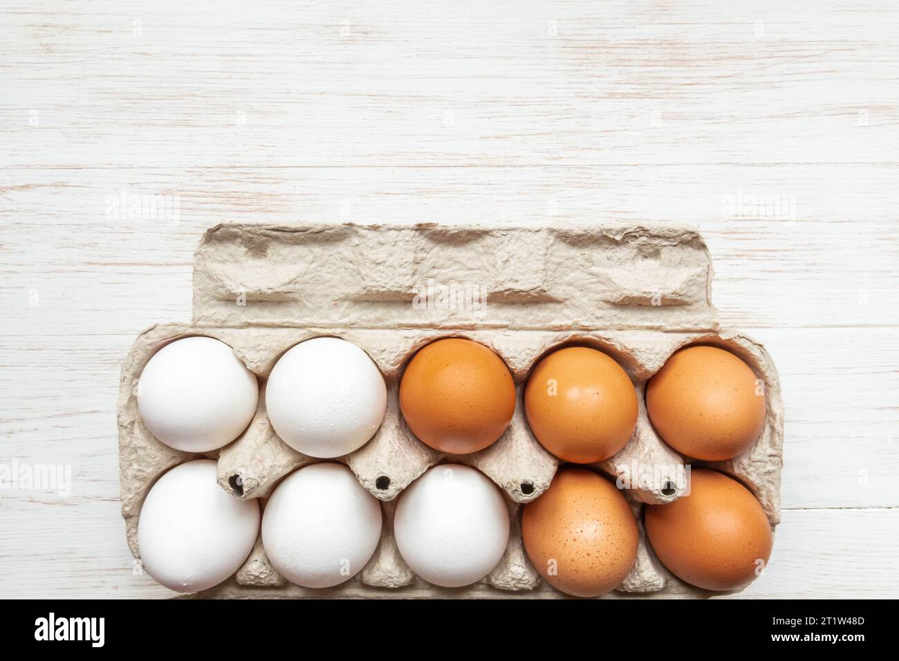 Brown and white eggs in open carton box. Fresh organic chicken eggs in carton pack on wooden surface. Top view with copy space. Natural healthy food a Stock Photo